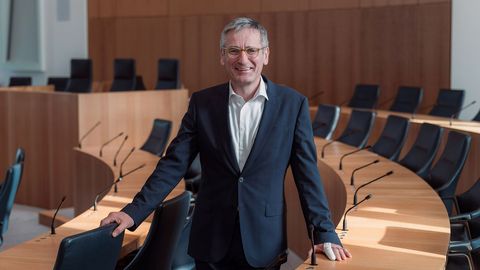 Landtagspräsident  Hendrik Hering im Plenarsaal des Deutschhauses; der Präsident steht zwischen zwei Sitzreihen; er lächelt, die Stimmung ist locker; im Hintergrund ist das Rednerpult zu sehen