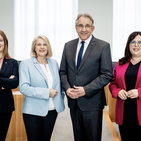 Zu sehen sind vier Personen nebeneinanderstehend im Rund des Plenarsaals.