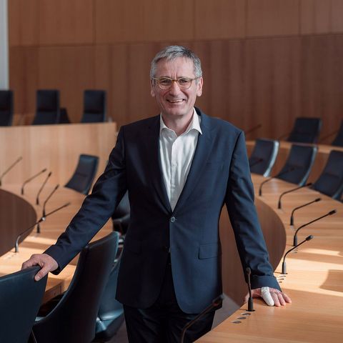 Landtagspräsident  Hendrik Hering im Plenarsaal des Deutschhauses; der Präsident steht zwischen zwei Sitzreihen; er lächelt, die Stimmung ist locker; im Hintergrund ist das Rednerpult zu sehen