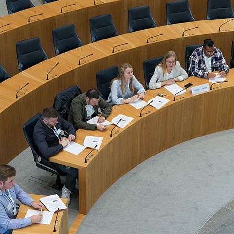 Die Teilnehmenden sitzen während den Debatten auf den Stühlen der Abgeordneten im Plenarsaal (Vogelperspektive).