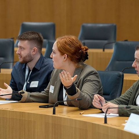 Die Teilnehmenden sitzen während den Debatten auf den Stühlen der Abgeordneten im Plenarsaal.