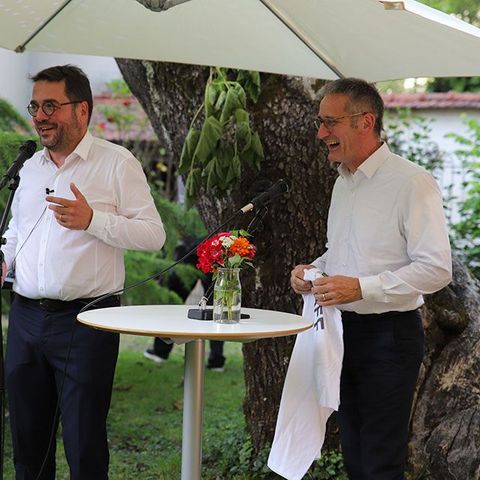 Die besagten Personen halten eine Rede. Vor ihnen sind zwei Mikrofone aufgebaut.