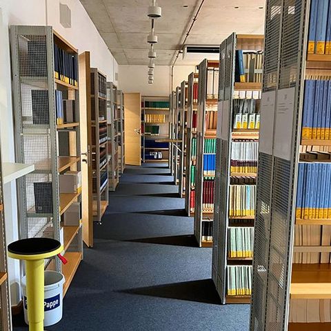 Ein breiter Gang führt zwischen mehreren Reihen von Bücherregalen hindurch.