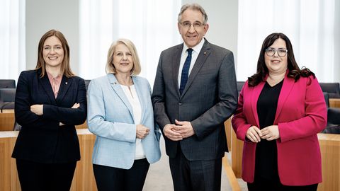 Zu sehen sind vier Personen nebeneinanderstehend im Rund des Plenarsaals.