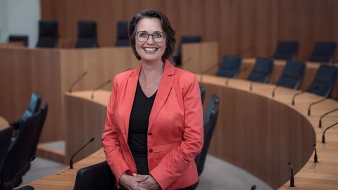Die Vizepräsidentin des Landtags Rheinland-Pfalz, Kathrin Anklam-Trapp. Das Foto ist horizontal ausgerichtet. Die Vizepräsidentin steht lächelnd zwischen den Stuhlreihen des Plenarsaals.