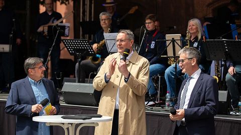 Der Ministerpräsident spricht in ein Mikrofon. Der Landtagspräsident und der Leiter der Blue Light Big Band des Polizeipräsidiums Ludwigshafen stehen neben ihm.