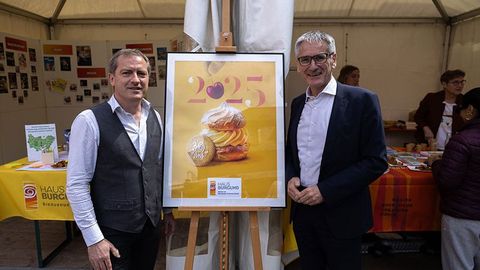 Landtagspräsident Hendrik Hering steht mit einer weiteren Person vor dem Stand. Zwischen ihnen befindet sich das gerahmte Plakat zum 30jährigen Bestehen des Hauses Burgund.