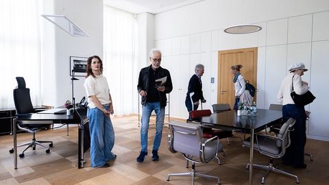 Auf dem Bild sieht man eine Gruppe von Personen im Präsidentenzimmer des Landtags Rheinland-Pfalz. Der Raum ist hell und großzügig gestaltet, mit großen Fenstern, die viel Tageslicht hereinlassen.  Auf der linken Seite steht ein eleganter Schreibtisch mit einem schwarzen Drehstuhl, einer Blumenvase und einem Telefon.  In der Mitte befindet sich ein großer Konferenztisch mit mehreren modernen Stühlen, auf dem Tisch stehen Wasserkaraffen und Gläser.  An der Wand sind große Schranktüren in einem minimalistischen Design zu sehen.