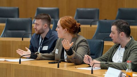 Die Teilnehmenden sitzen während den Debatten auf den Stühlen der Abgeordneten im Plenarsaal.