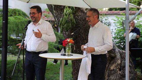 Die besagten Personen halten eine Rede. Vor ihnen sind zwei Mikrofone aufgebaut.
