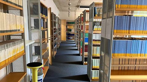 Ein breiter Gang führt zwischen mehreren Reihen von Bücherregalen hindurch.