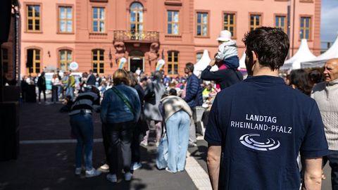 Im Vordergrund steht ein Mann mit einem dunkelblauen T-Shirt, auf dessen Rückseite die Aufschrift 