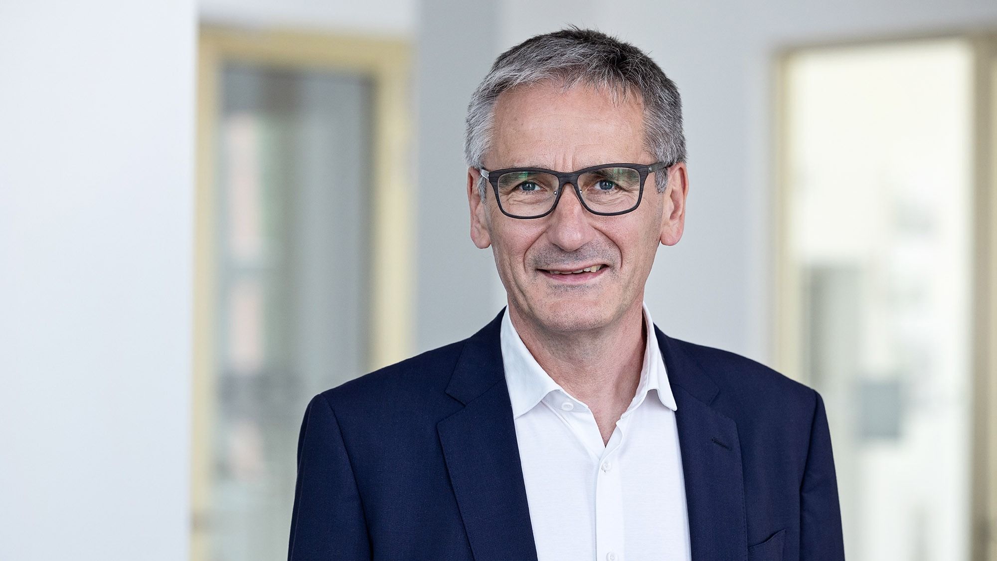 Landtagspräsident Hendrik Hering lächelt. Er steht vor einem Fenster. Das Bild wirkt hell und licht.