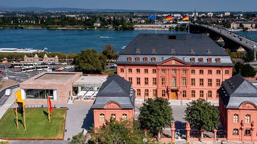 Luftaufnahme des Deutschhauses an einem sonnigen Tag. Im Hintergrund ist der Rhein zu sehen.