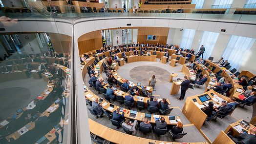 Der gefüllte Plenarsaal von der Zuschauertribüne aus. Spiegelung des Saals an der Glasbrüstung der Empore. Das 7. Plenum ist zugleich die 1. Plenarsitzung im sanierten Deutschhaus.