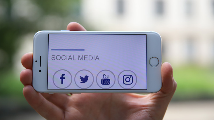 Hand hält ein Smartphone - darauf zu sehen sind Social Media Logos 