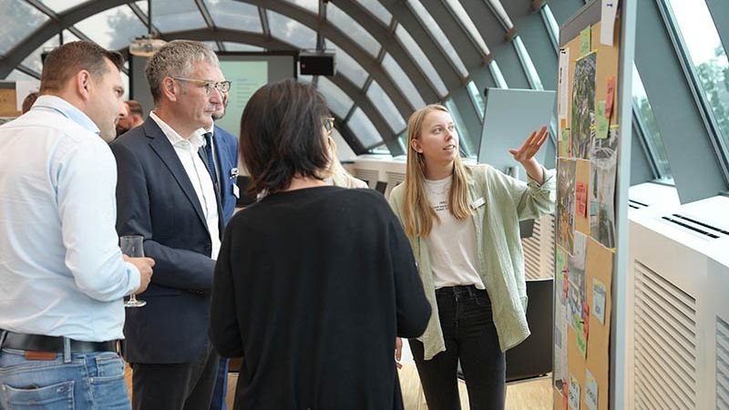 Die Teilnehmer und Teilnehmerinnen erhalten Informationen, stehend vor einer Pinnwand.
