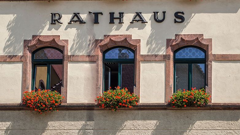 Symbolbild Rathaus. Zu sehen ist der Ausschnitt einer Gebäudefront mit der Aufschrift "Rathaus". Mobilansicht