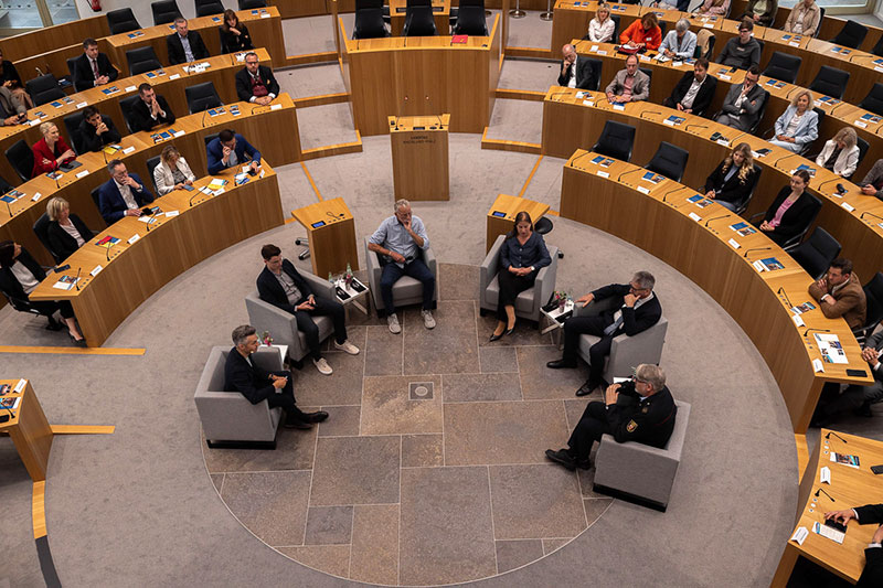 Das Bild zeigt von der Tribüne aus die Gäste der Talk-Runde im Plenarsaal. Blick von oben in das Plenarrund.
