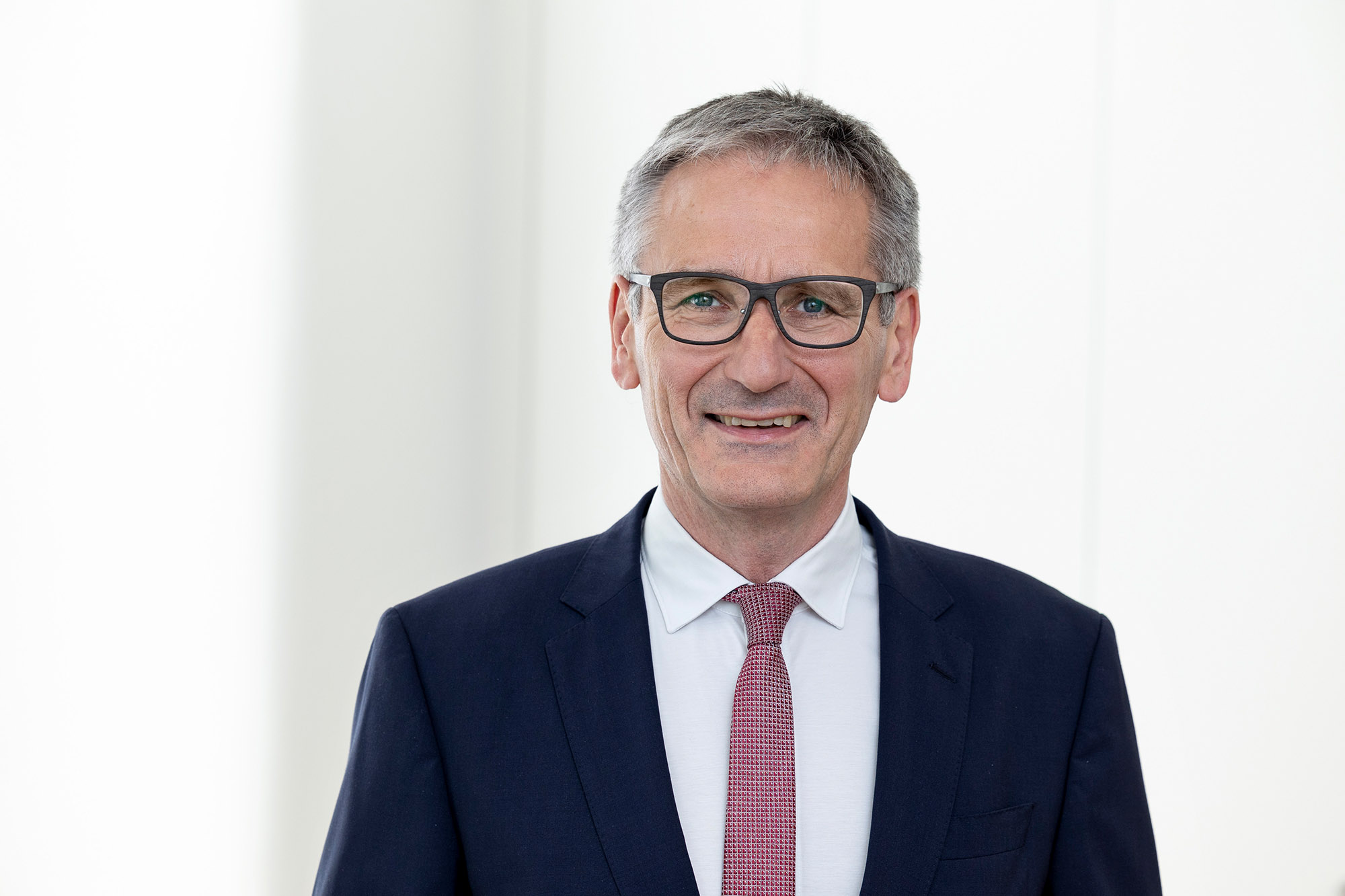 Landtagspräsident Hendrik Hering lächelt. Er steht vor einem Fenster. das Bild wirkt hell und licht.