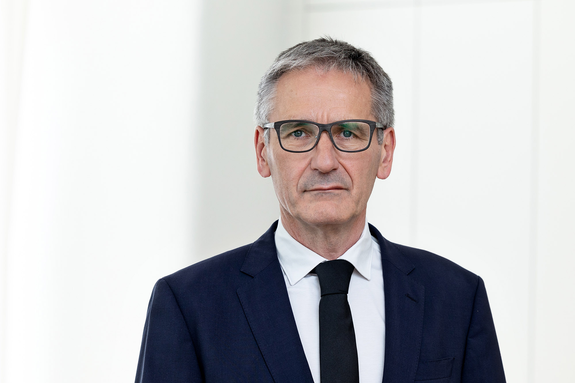 Landtagspräsident Hendrik Hering mit ernstem Gesichtsausdruck. Er steht vor einem Fenster. das Bild wirkt hell und licht.