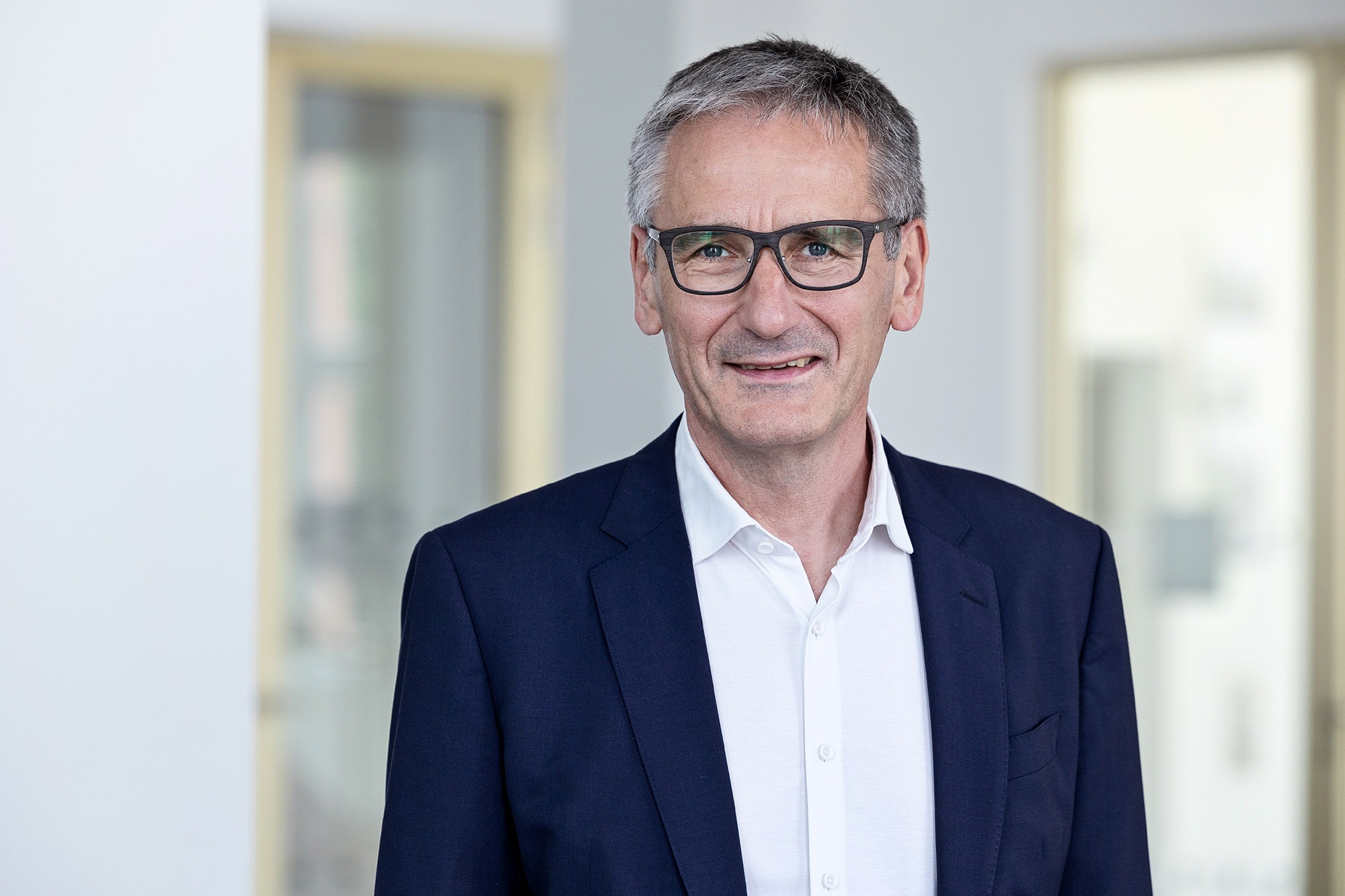Landtagspräsident Hendrik Hering lächelt. Er steht vor einem Fenster. Das Bild wirkt hell und licht.