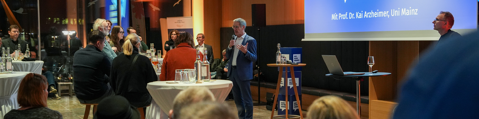 Zu sehen sind mehrere Personen. Sie befinden sich im Esszimmer des Landtags und hören gespannt dem Redner zu. 