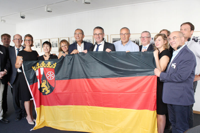 Eine Delegation aus der Partnerregion Burgund-Franche-Comté im Haus Burgund in Mainz; die Teilnehmer halten die rheinland-pfälzische Flagge.