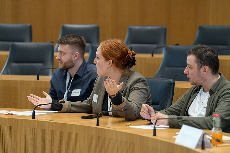 Die Teilnehmenden sitzen während den Debatten auf den Stühlen der Abgeordneten im Plenarsaal.