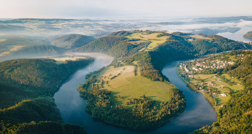 Zu sehen ist eine Landschaft mit einer beeindruckenden Flussschleife. Diese Flussschleife ist umgeben von dichten Wäldern und sanften Hügeln.