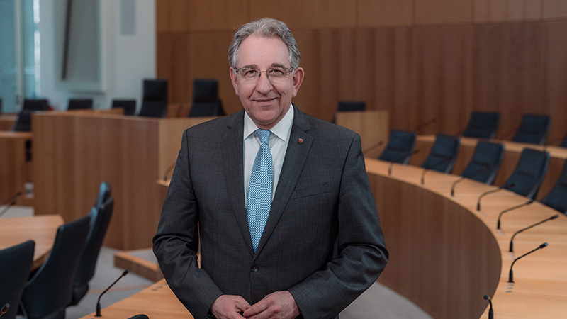 Zu sehen ist ein Mann stehend im leeren Plenarsaal