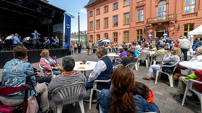 Die Gäste sitzen im Hof des Deutschhauses an verschiedenen Tischgruppen vor einer großen Bühne auf der Musik gespielt wird.