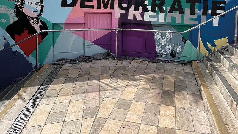 Zu sehen ist eine Graffitiwand. Viele bunte Farben, linke Seite eine schwarz-wei&szlig; Kontur eines Mannes. Quer dar&uuml;ber steht in gro&szlig;em Buchstaben: Demokratie Freiheit